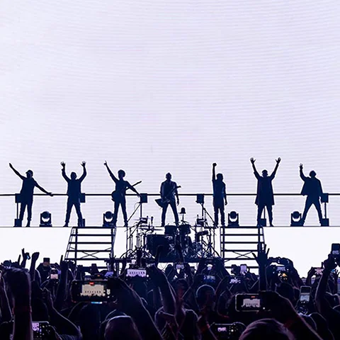 Silhueta da banda Titãs no palco com painel de led com fundo branco atrás